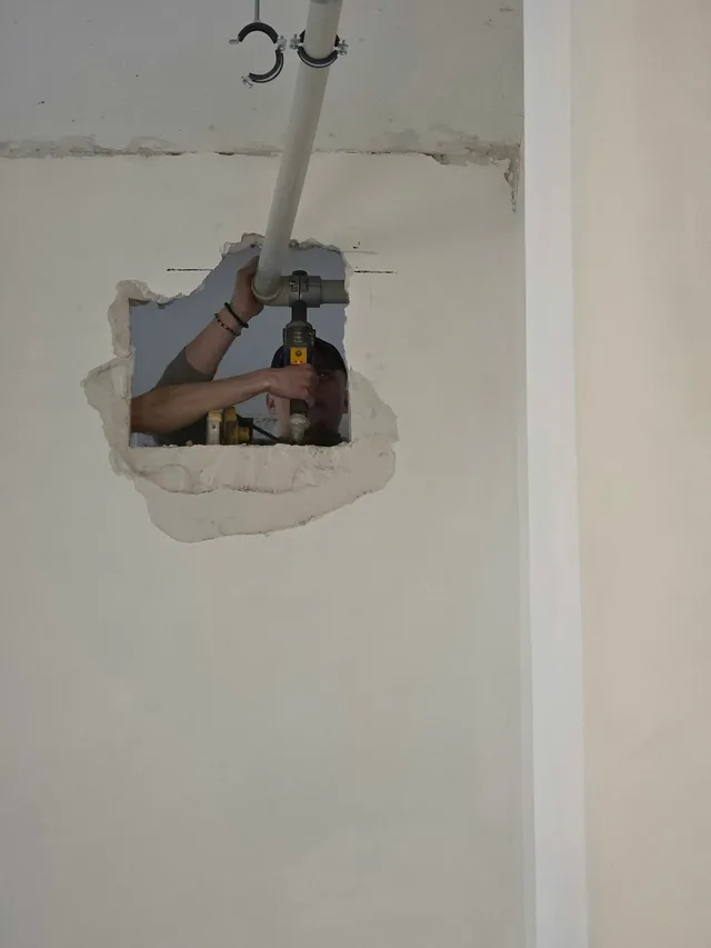 Ruka nasazuje armaturu na potrubí v probouraném prostupu ve stěně
