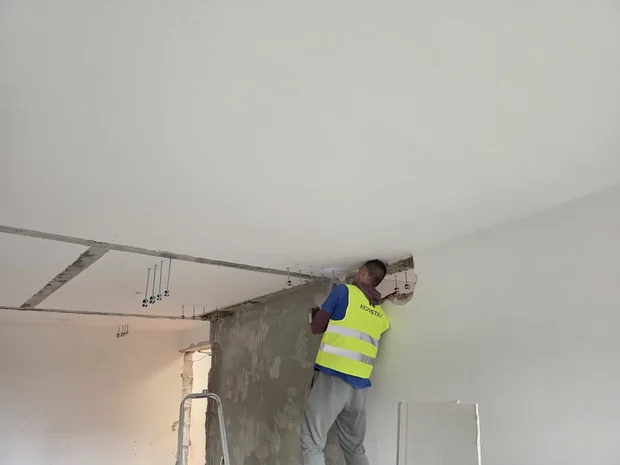 Montér ve vestě pracuje na prostupu ve stěně těsně pod stropem, vedle vyvedené vývody rozvodů