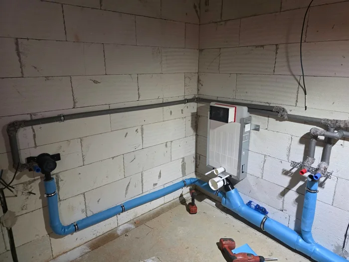 Roh bytového jádra s&nbsp;předstěnovým modulem WC, modrým odpadním potrubím a&nbsp;vývody vody