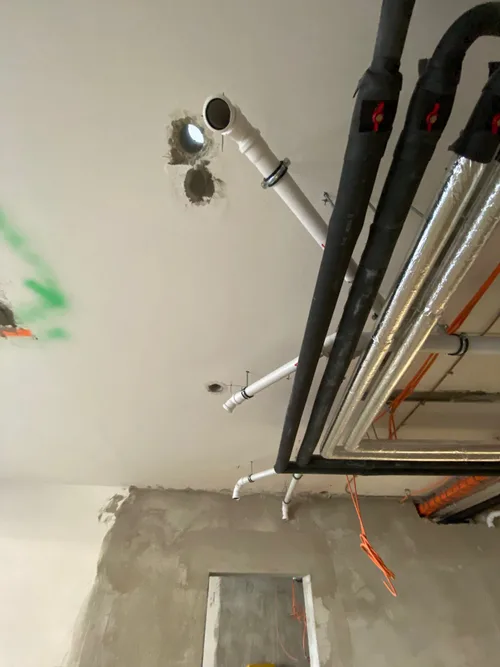 Odpadní potrubí vyvedené ze stropu vedle izolovaných rozvodů topení