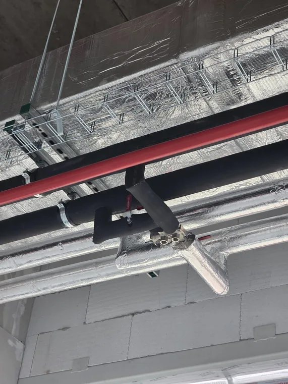 Izolované rozvody vody a topení vedené pod betonovým stropem nad kabelovými žlaby