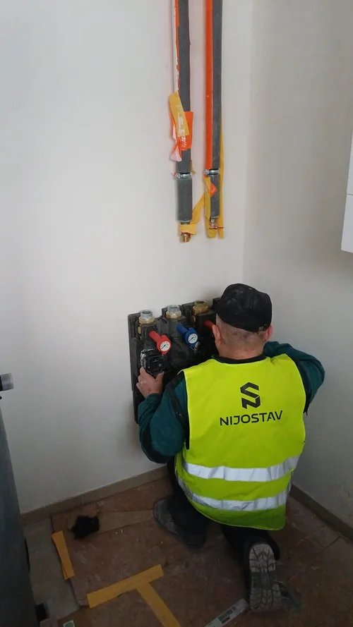 Montér ve vestě NIJOSTAV montuje čerpadlovou skupinu na stěnu